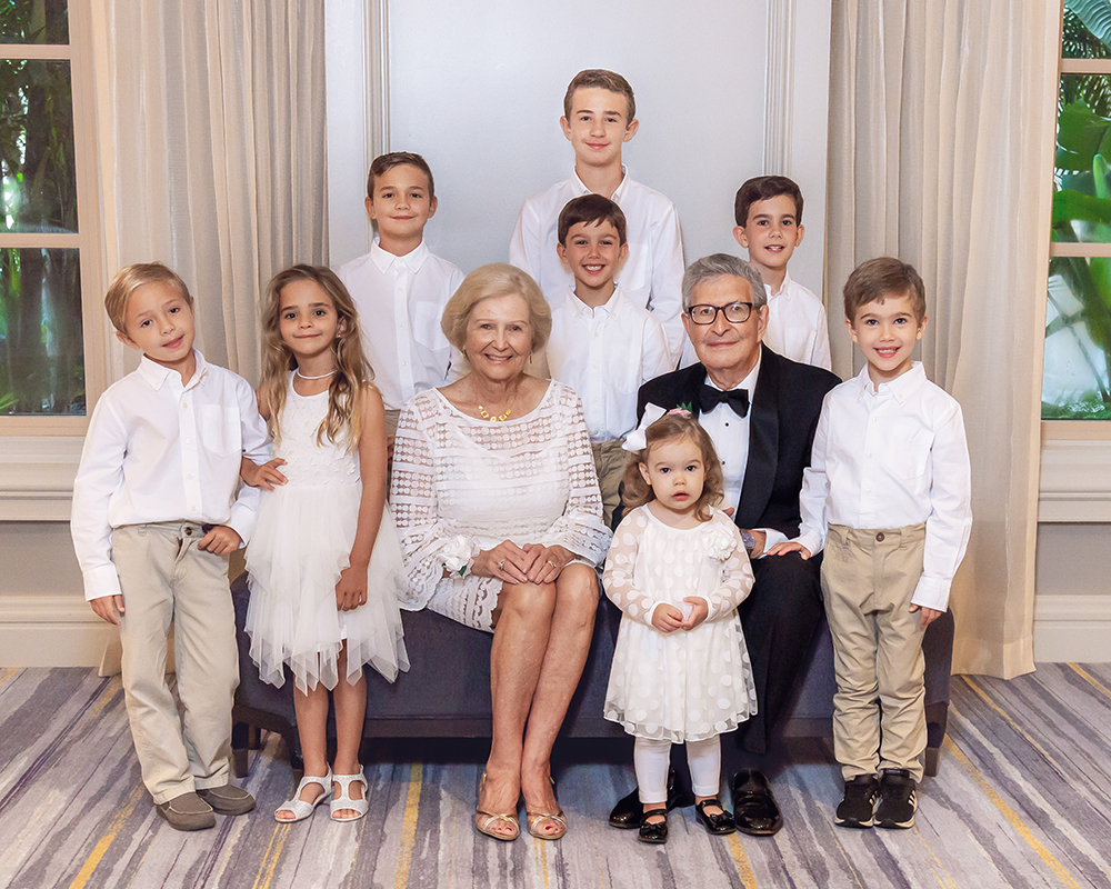grandparents seated on a couch with eight grandchildren standing around them and smiling
